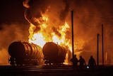 Residents watch tank cars set ablaze following recent shelling at a railway junction.