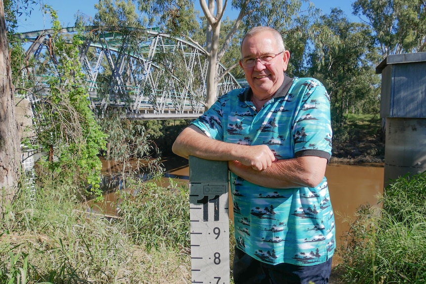 A man stands next to a flood height marker next to a river