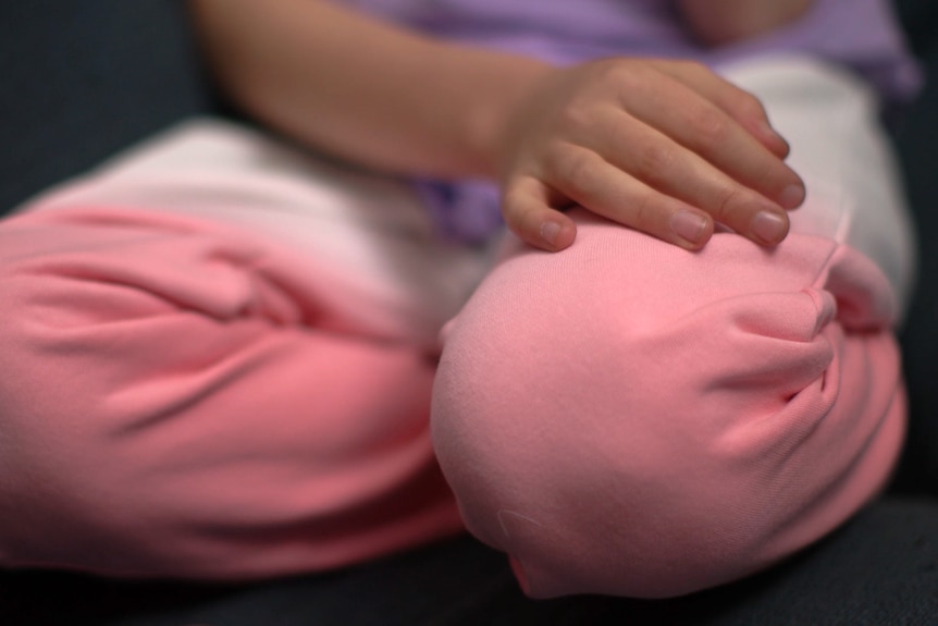 An unidentifiable child rests their hand on their leg. Only their leg and hand are in focus.