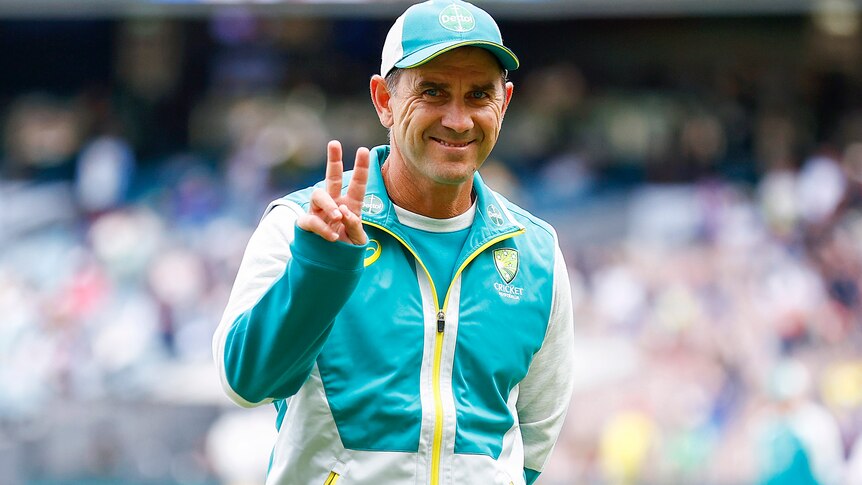 Justin Langer smiles and gives the peace sign to the camera