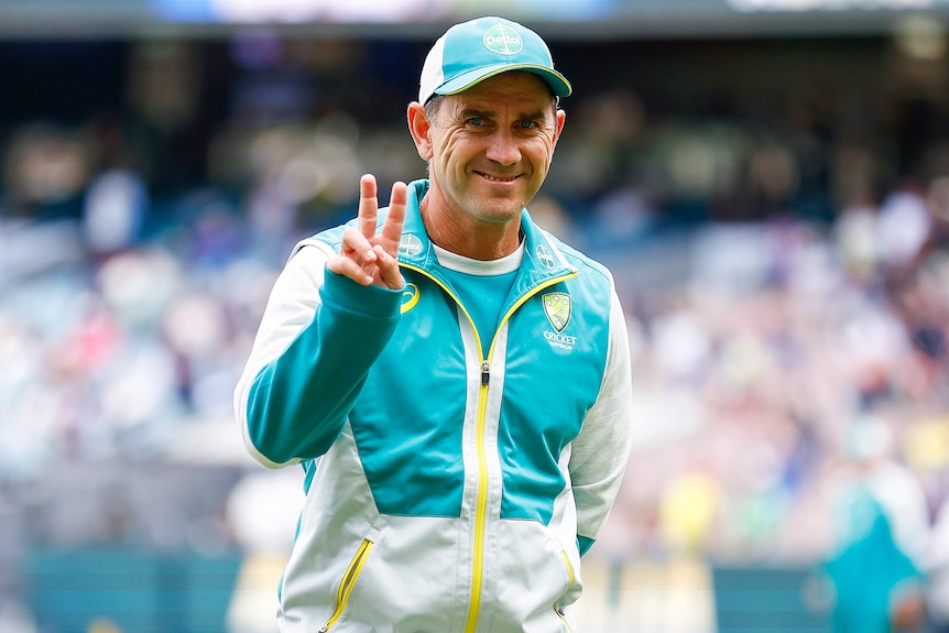 Justin Langer smiles and gives the peace sign to the camera