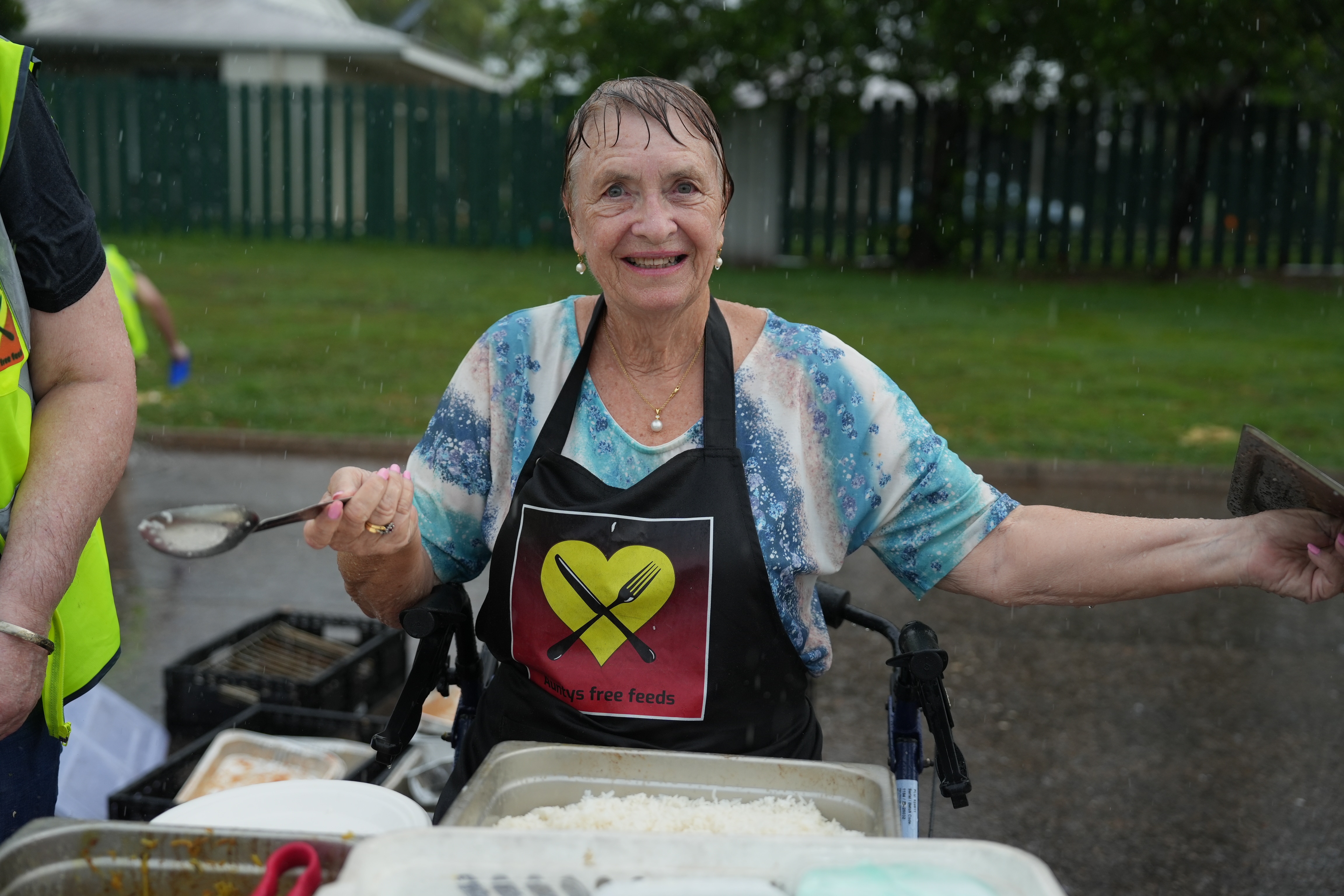 A volunteer serves food to diners in the rain.