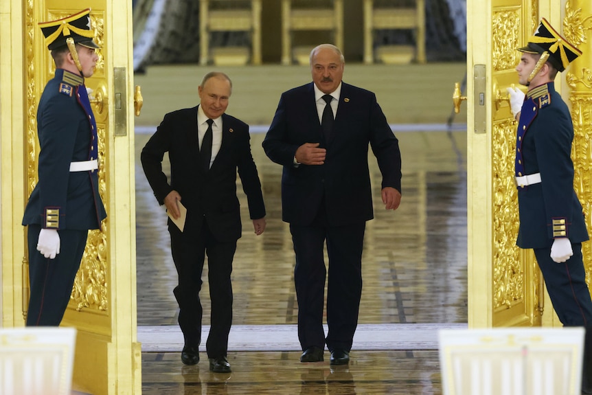 Vladimir Putin and Alexander Lukashenko walk through a door armed by guards.