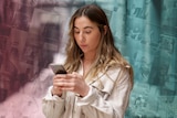 Lauren looks at her phone. Behind her is a pink and blue background showing dozens of TikTok videos.