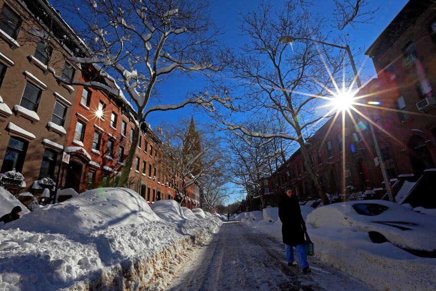 A woman walks down a snow covered street in Brooklyn, New York City.