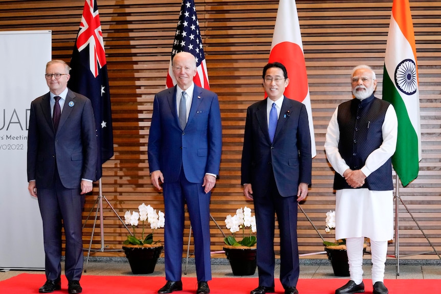 Anthony Albanese, Joe Biden, Fumio Kishida 및 Narendra Modi가 깃발 앞에서 미소를 지으며 줄을 서고 있습니다. 