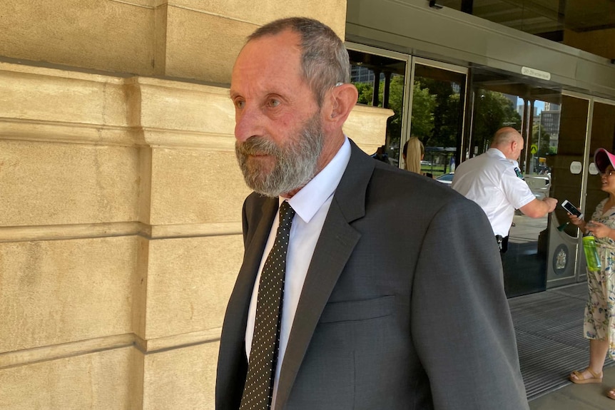 An older man with a beard wearing a suit outside a court.