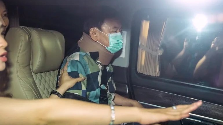 An elderly man wears green face mask in car as photographers outside use flash cameras