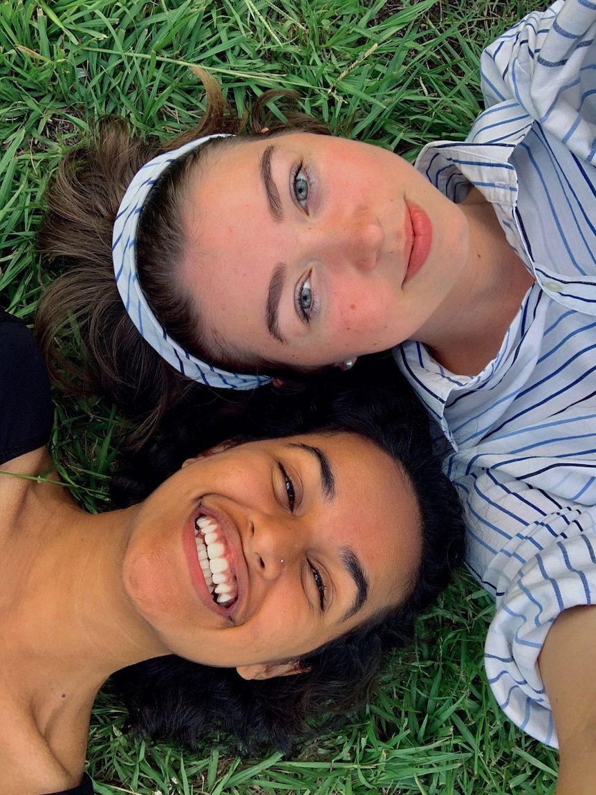 Shanu Sobti and India Cavenagh take a headshot selfie while laying on the grass at school.