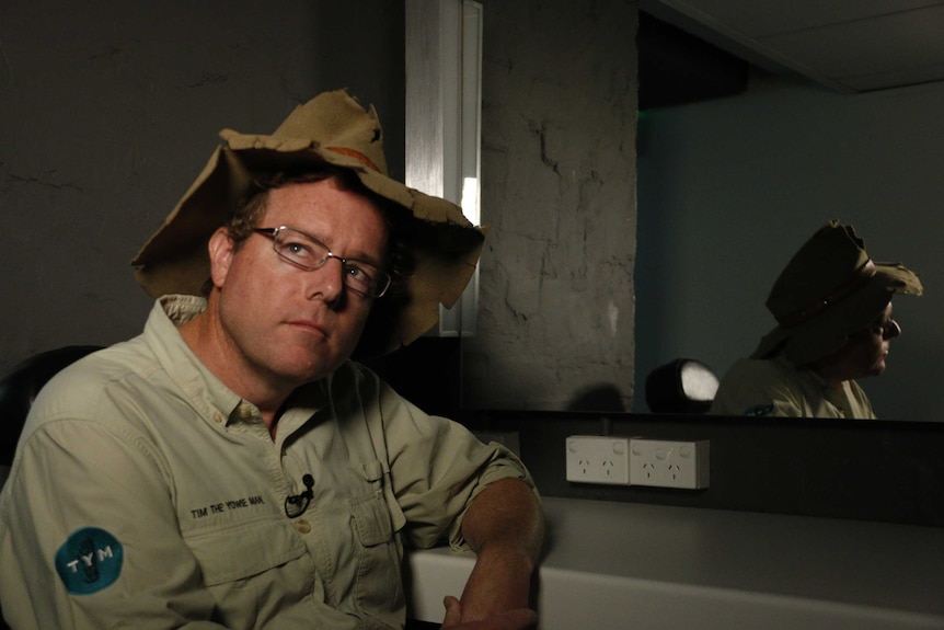 Tim the Yowie Man, in a tattered Akubra hat, in front of a mirror.