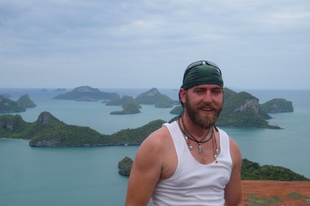 A smiling young man stands in front of a ocean sweeping vista dotted with islands.