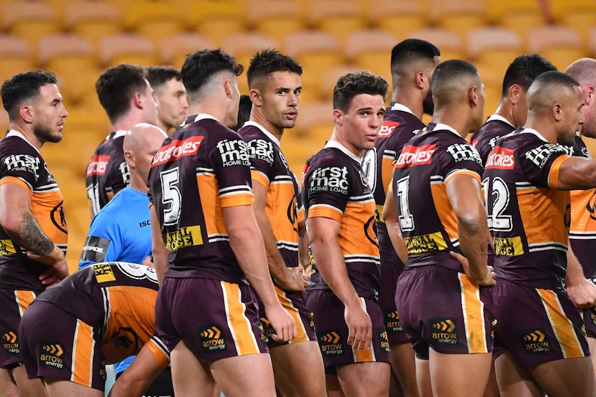 Brisbane Broncos NRL players look dejected as they stand in a group next to goal posts against the Sydney Roosters.