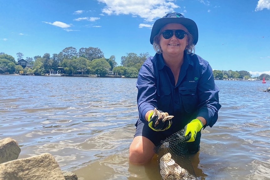 woman standing in river with hat and sunnies on holding oysters