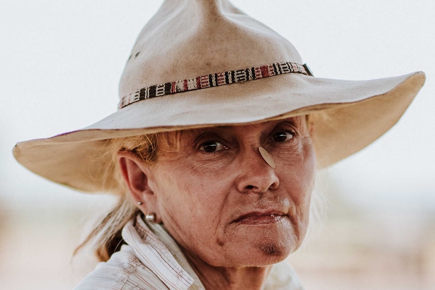 Close up image woman in broad rimmed hat, with dirt on face.