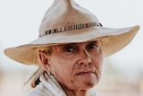 Close up image woman in broad rimmed hat, with dirt on face.