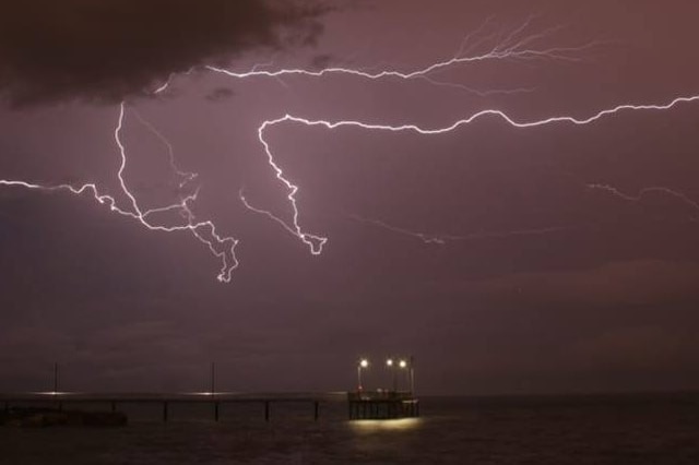 Lightning cracks above Nightcliff Jetty, just outside Darwin. The sky is a warm red.