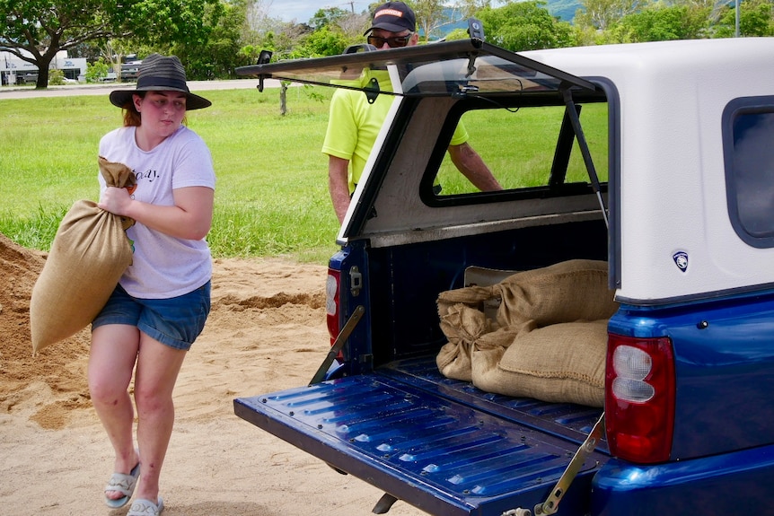 a young girl carrying a large sandbag to the tray of a ute