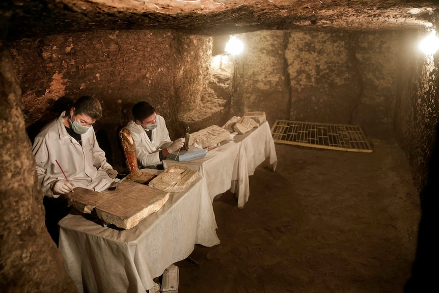 Archaeologists work on statues and artefacts inside a tomb.