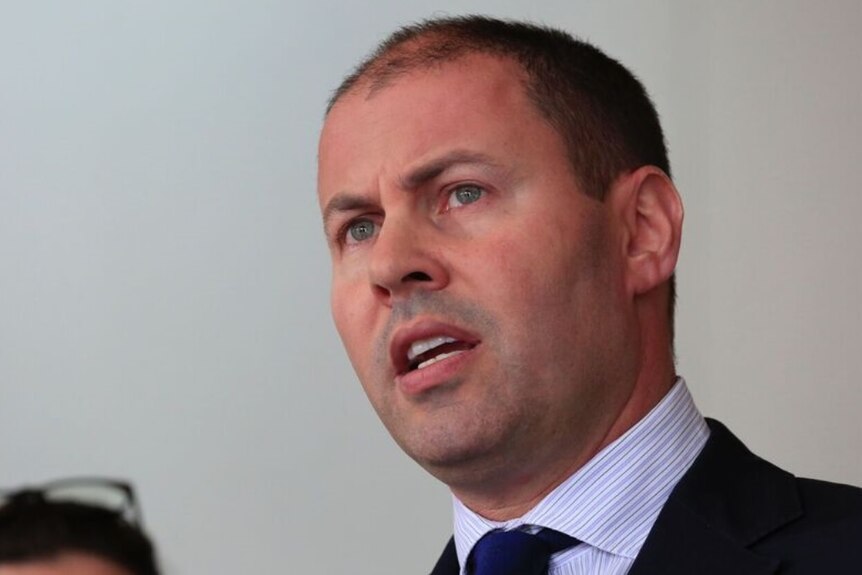 Josh Frydenberg, shot from slightly below, speaks at a press conference. He has a sincere expression on his face.