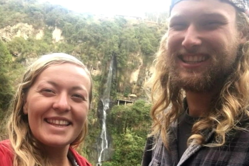 A woman and man standing in front of a waterfall.
