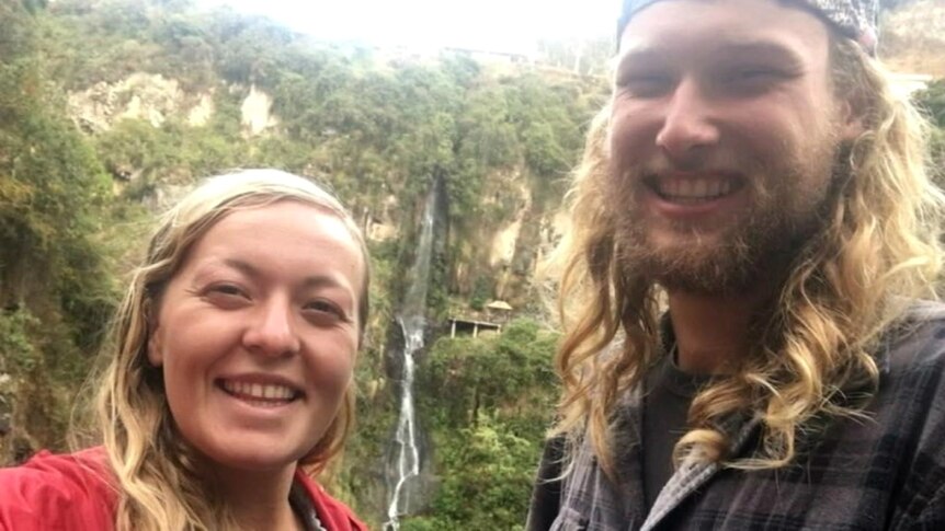 A woman and man standing in front of a waterfall.