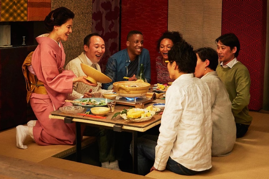 A Japanese family sits down with their guests and has a traditional dinner with them.