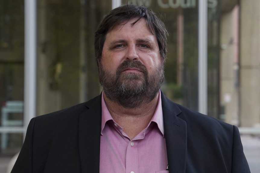 A front-on portrait of a man in front of the law courts.