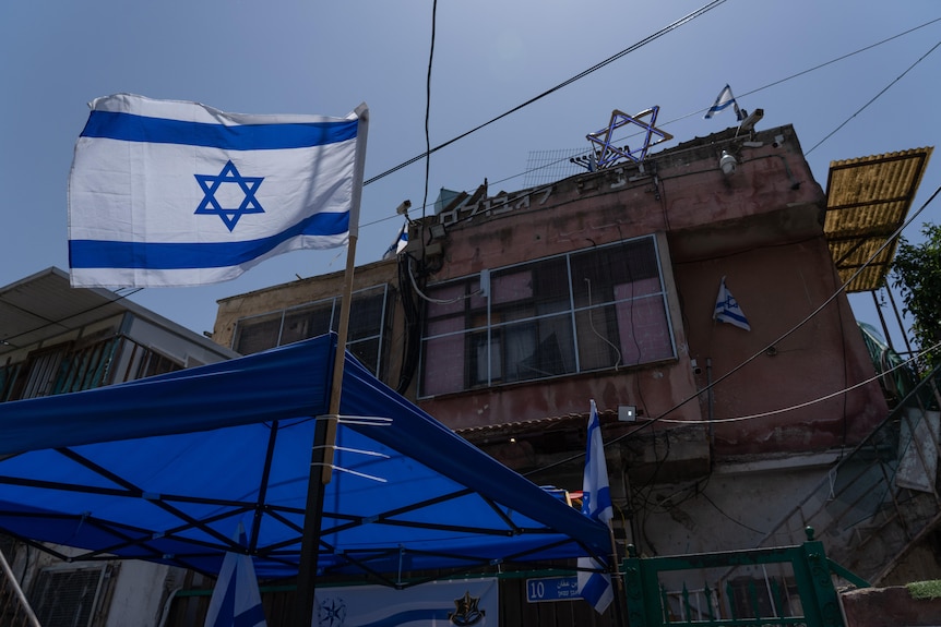 An Israeli flag flutters above a brown building  