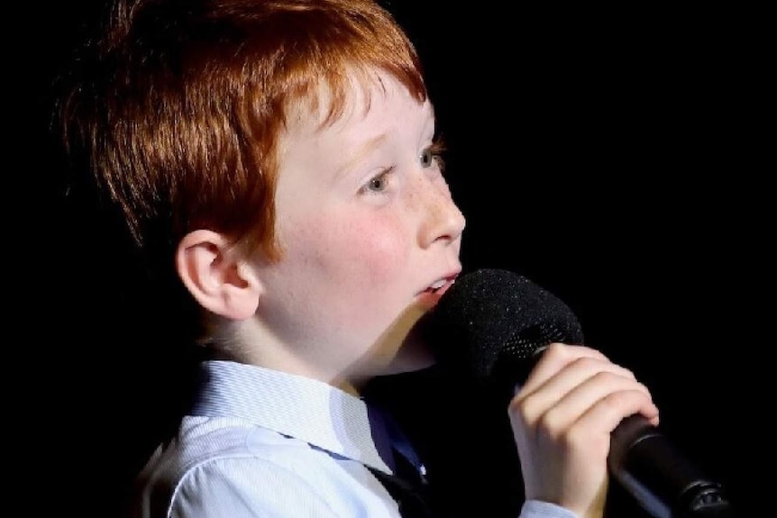 Ethan holds a microphone as he sings.