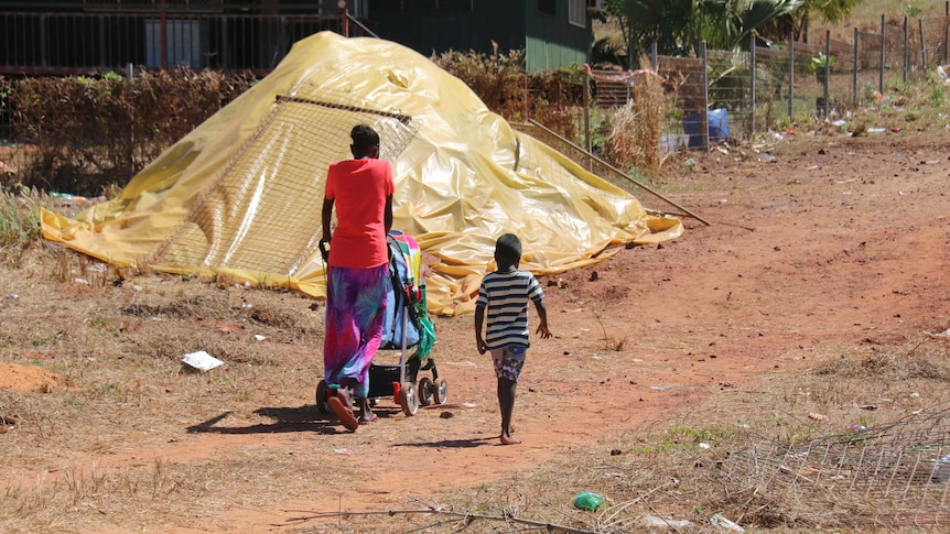 A woman and child walk past a covered pile of soil or debris left behind after a building demolition in Galiwin’ku.