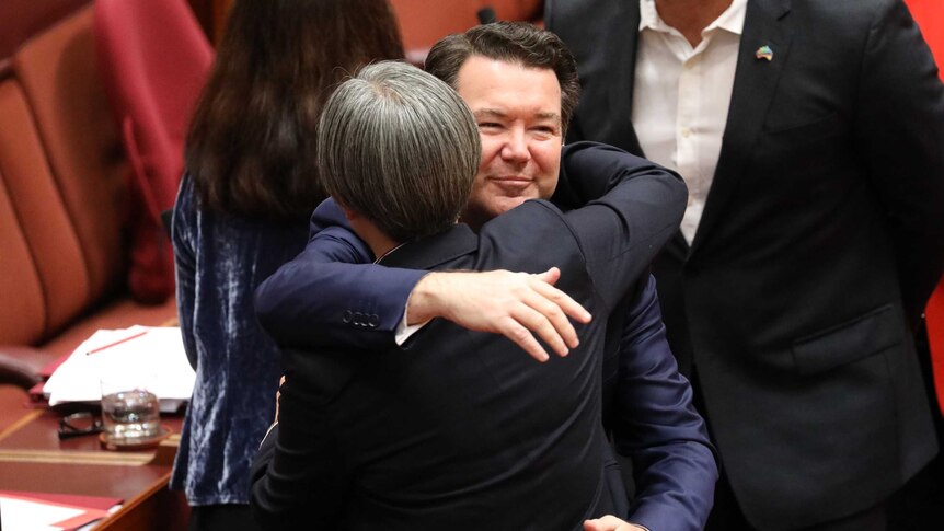 Dean Smith smiles while hugging Penny Wong. Behind him there are other senators lining up to embrace him