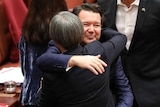 Dean Smith smiles while hugging Penny Wong. Behind him there are other senators lining up to embrace him