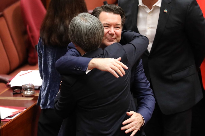 Dean Smith smiles while hugging Penny Wong. Behind him there are other senators lining up to embrace him