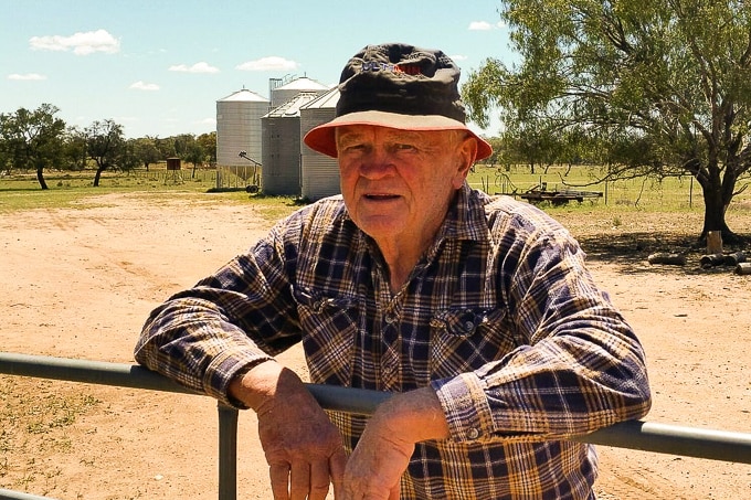 Gilgandra farmer Jim Claringbold leans on his farm gate, silos can be seen in the background