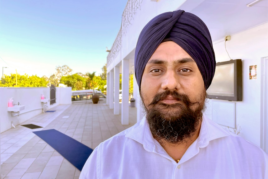 A man in Sikh headdress stands smiling outside his temple.