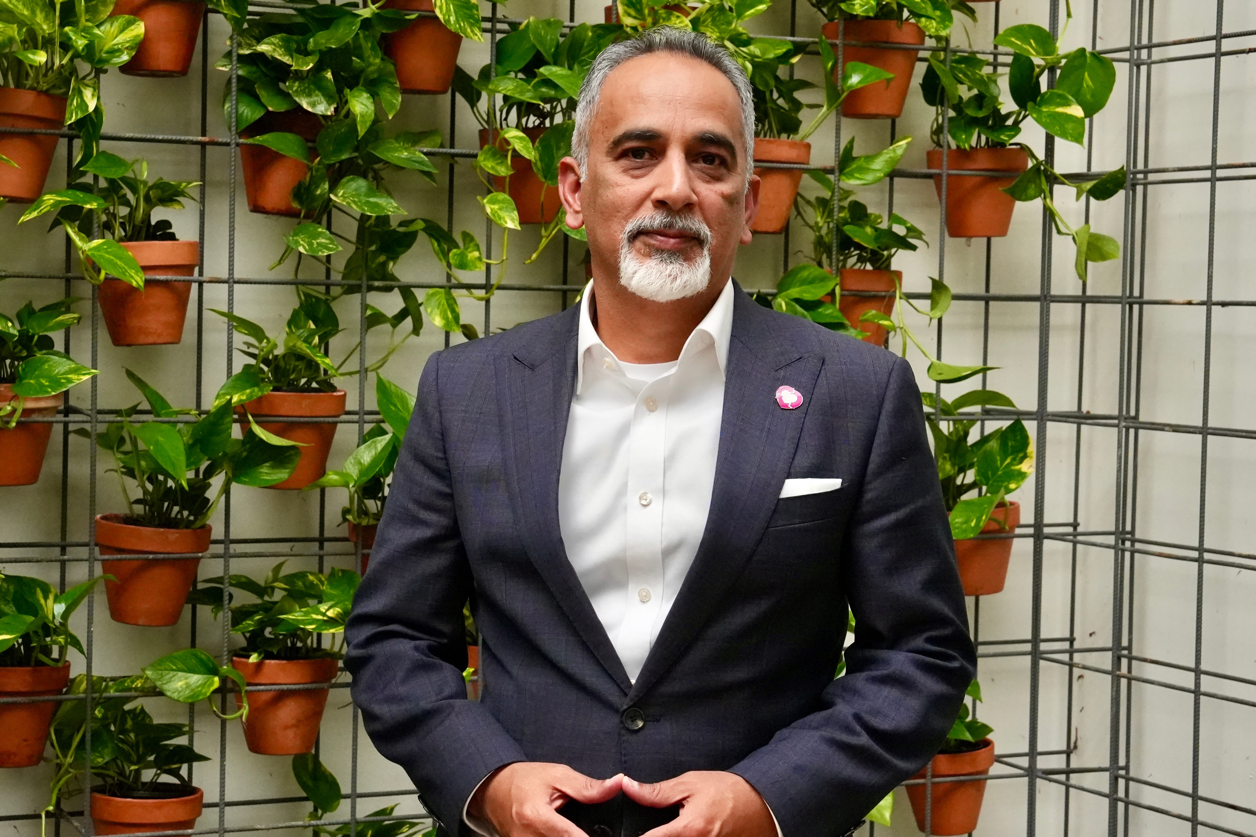 A man with short black hair stands outdoors wearing a navy suit with an organ donor sticker on the lapel.