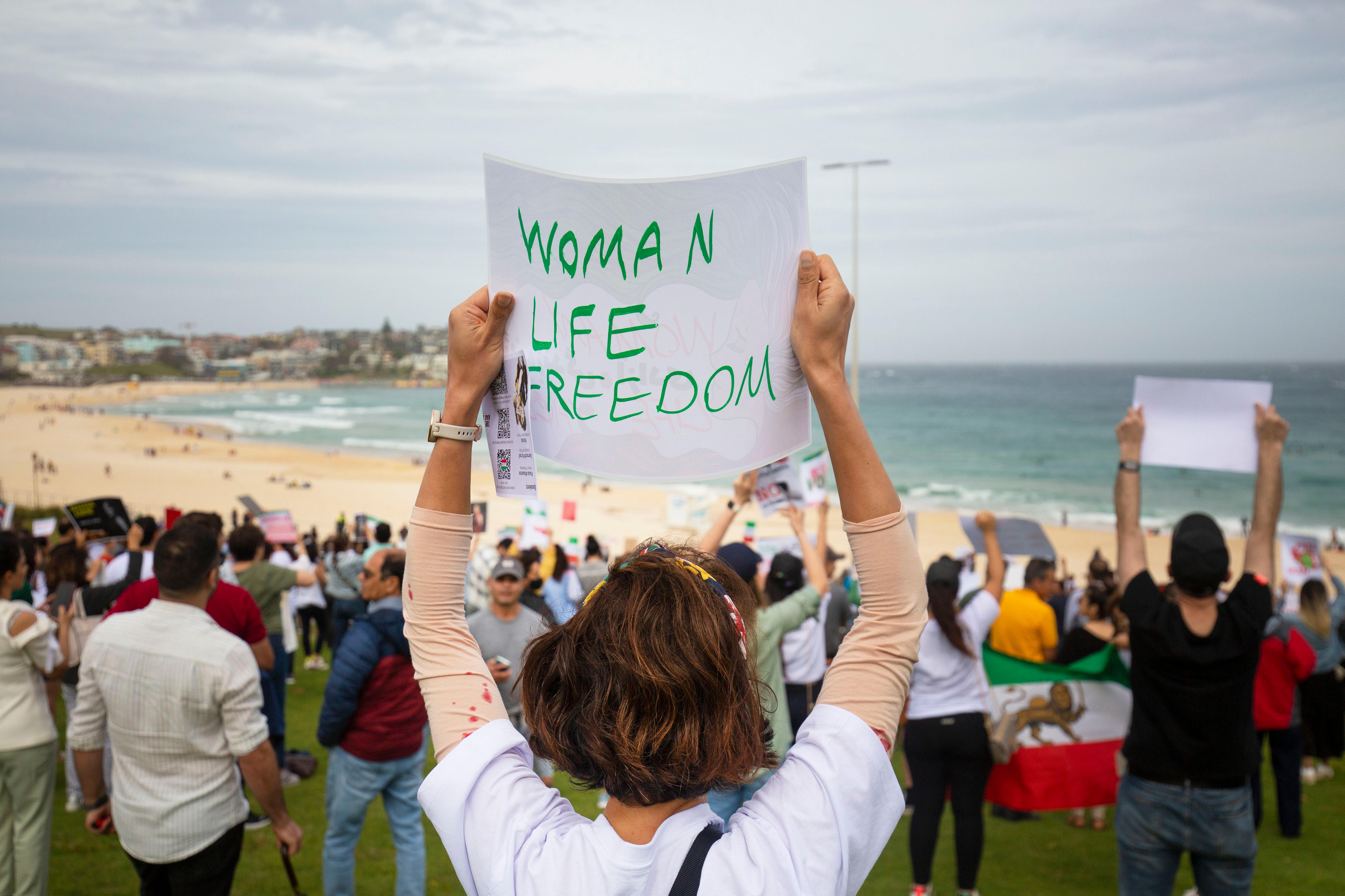 一名身穿白衬衫的妇女在邦迪海滩举行的抗议活动中举着写着“妇女生命自由”的标语。” class=
