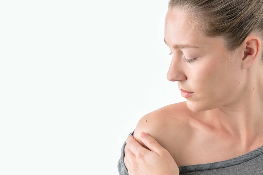 Women stares at mole on her shoulder.