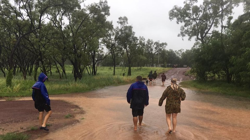 people and a dog walking through floodwaters.