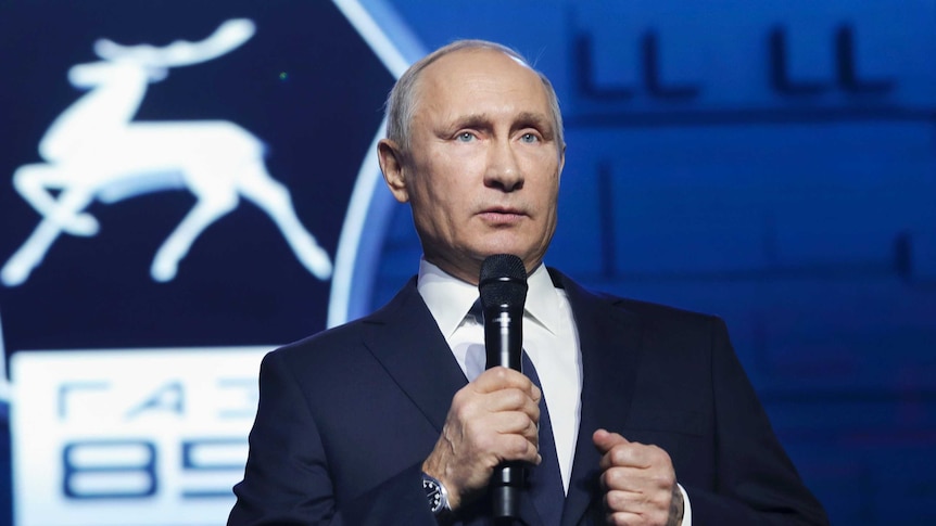 Russian President Vladimir Putin holds a microphone.