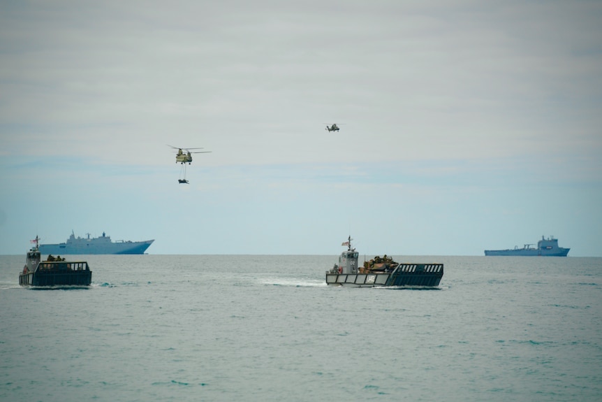 Australian warships and Army helicopters as well as landing craft are visible making a coordinated landing from sea to a beach.