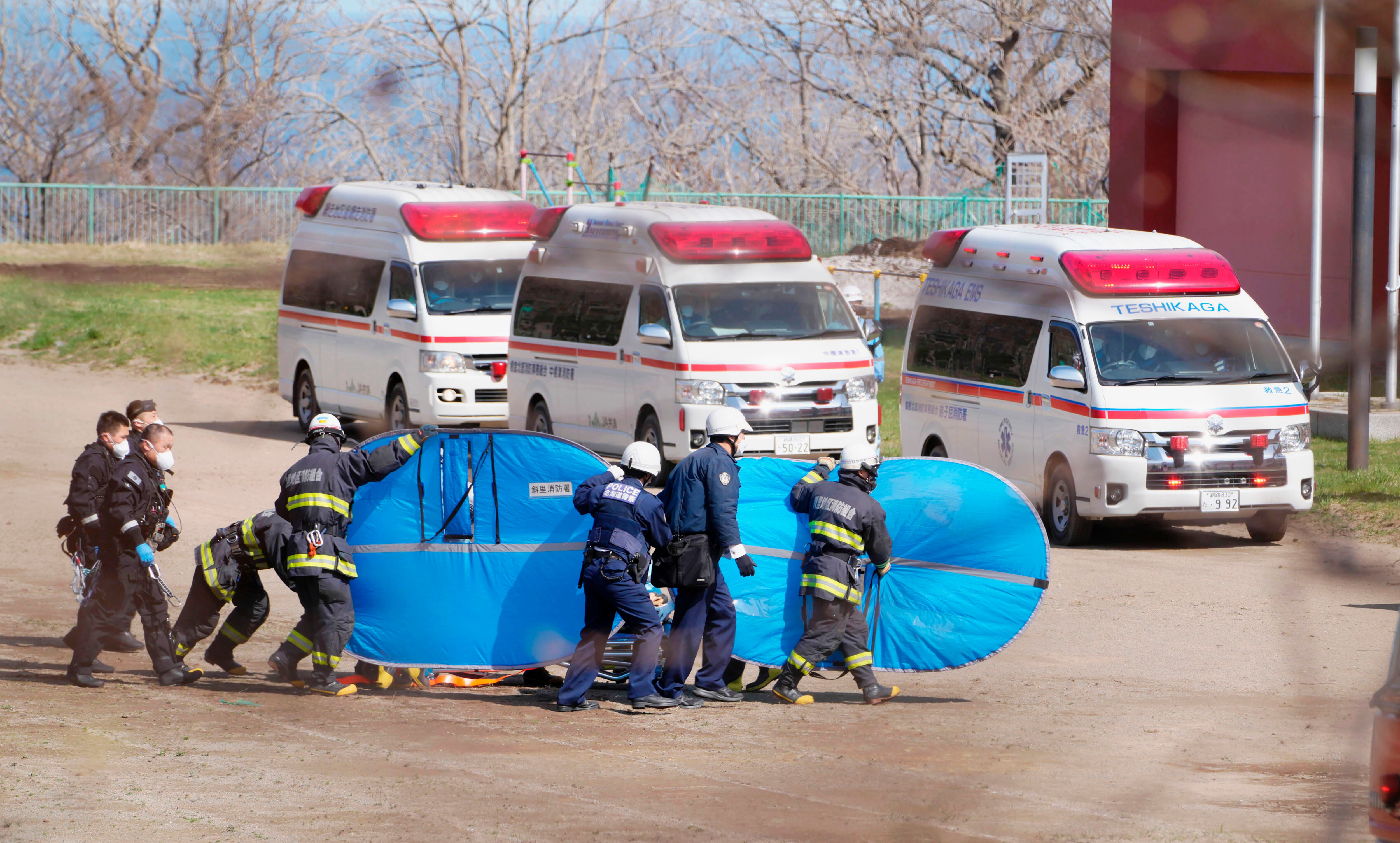A group of firefighters carry a large blue bag in front of 3 ambulances.