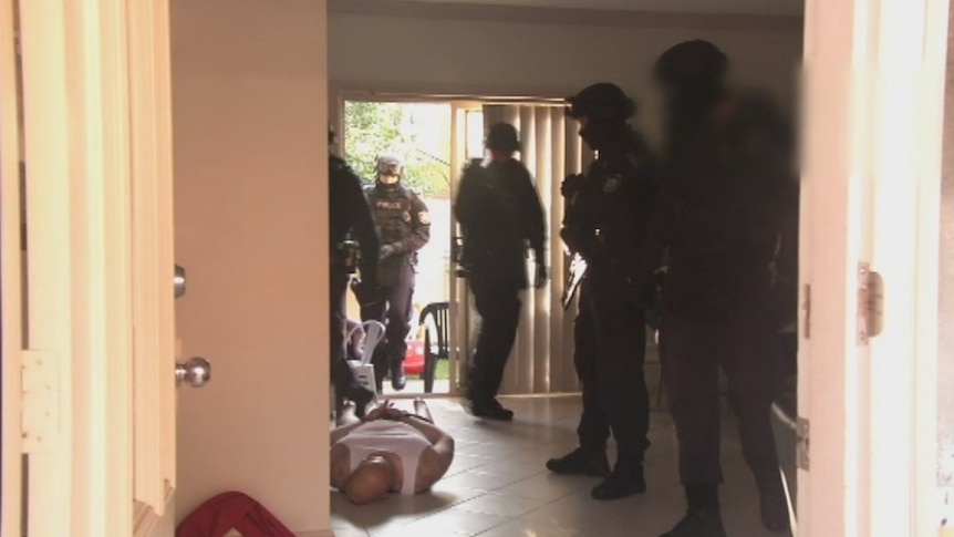 A handcuffed man lies face down, surrounded by officers during an early morning raid.