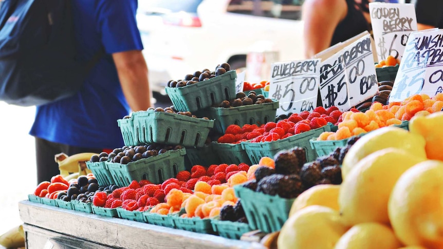 Fruit and vegetables for sale with man wearing backpack for a story about whether organic and local food is more sustainable