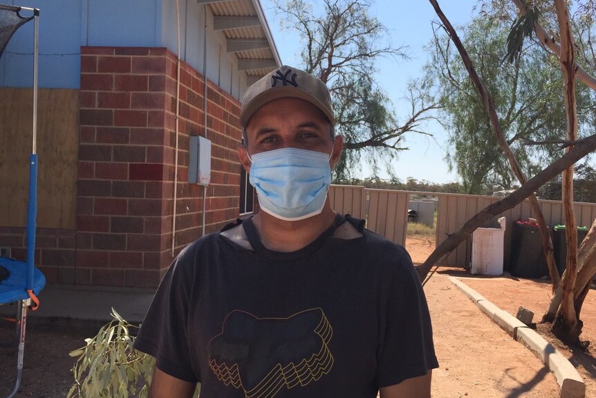 An Indigenous man wearing a mask and a cap standing outside.