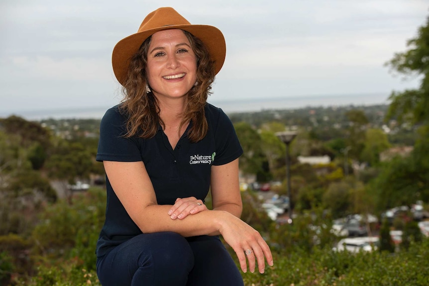 A woman in a hat smiles against a metropolitan ocean horizon.