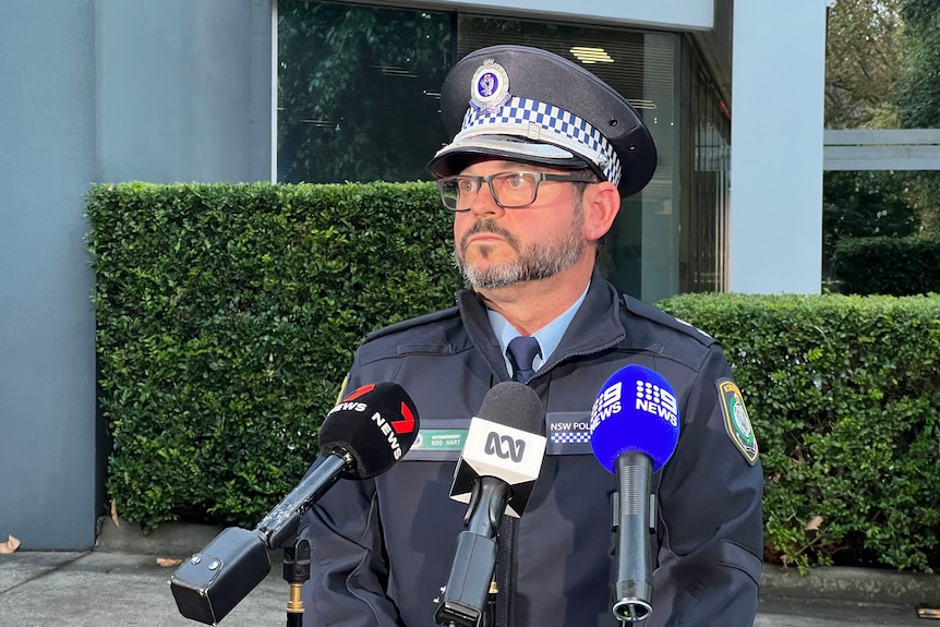 A police officer standing in front of a media conference with three microphones, 7 News, ABC and Nine News