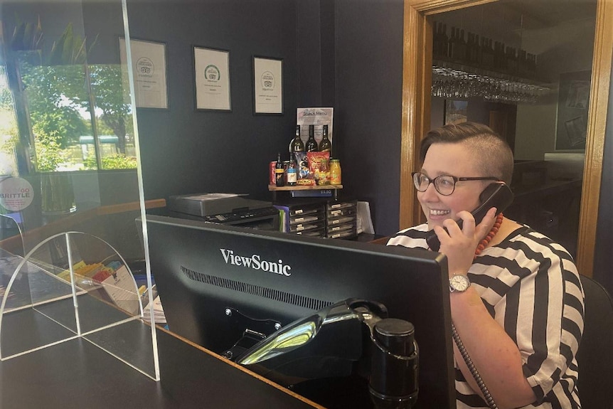 A woman sitting at a hotel desk, smiling while she talks on the phone.