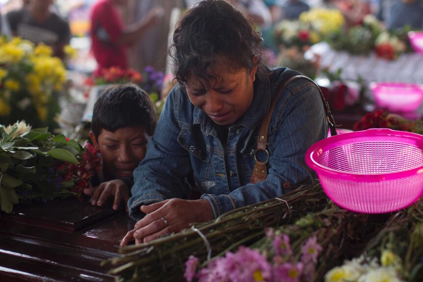 A woman and a boy cry over a coffin.