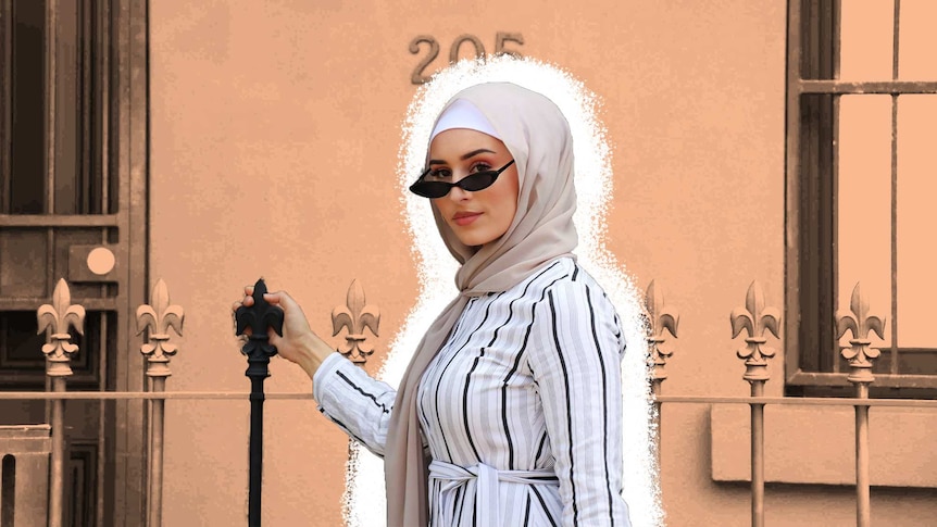 Hijabi model Nawal demonstrates a modest fashion look standing in front of a black building.